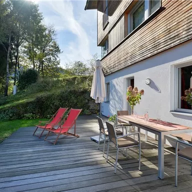 A cozy terrace with wooden decking and modern furniture.  
Red loungers and a dining table invite you to relax outdoors.