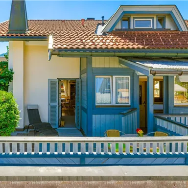 A pretty house with a red roof and blue walls. Cozy seating is located in front of the door.