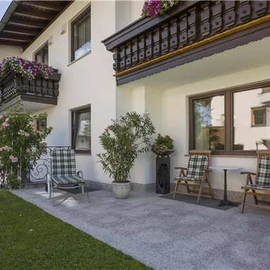 A modern house with a well-maintained garden. There are cozy chairs and flowers on the balconies, surrounded by mountains.
