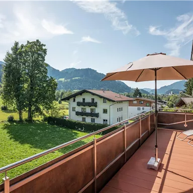 A beautiful balcony with a view of green meadows and mountains. Sun loungers and a sun umbrella provide for relaxed moments outdoors.
