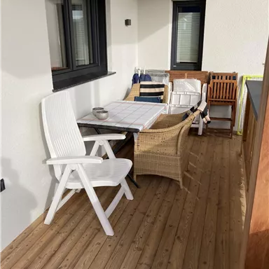 A cozy balcony with wooden decking and various seating options. The table is set and invites relaxation.