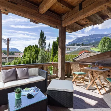 Eine gemütliche Terrasse mit Holzverkleidung und Blick auf die Berge. Es gibt einen Sitzbereich und einen Tisch mit Stühlen, um die Aussicht zu genießen.