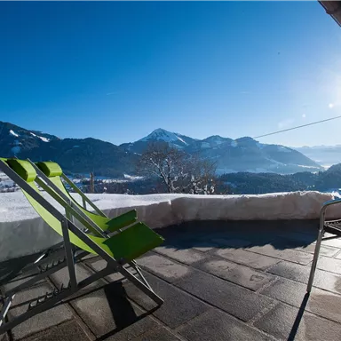 Eine sonnige Terrasse mit Liegestühlen und atemberaubendem Blick auf die Berge. Der Schnee glitzert in der Sonne, während der klare Himmel strahlt.