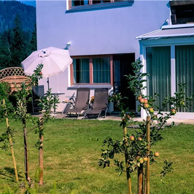 Ein ruhiger Garten mit einem modernen Haus im Hintergrund. Zwei Liegen und ein Sonnenschirm laden zum Entspannen ein.