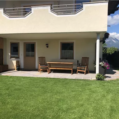Eine gemütliche Terrasse mit Holzmöbeln und einem gepflegten Rasen. Im Hintergrund sind die Berge zu sehen.