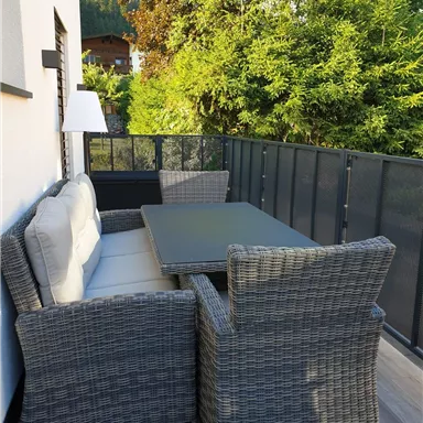 A cozy balcony with a modern rattan furniture set. The green surroundings create a relaxed atmosphere.