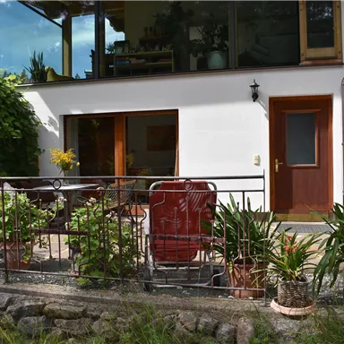 A beautiful living area with a terrace that is decorated with plants and furniture. A red umbrella provides shade.
