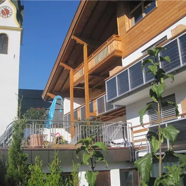 Ein modernes Gebäude mit Holzverkleidung und Solarpanelen. Im Hintergrund steht ein Kirchturm unter klarem Himmel.