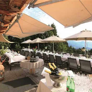 A stylish terrace with tables and chairs, set up for a celebration. Umbrellas provide shade and the view of the mountains is impressive.