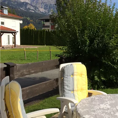 A beautiful garden with two lounge chairs and a table. In the background, mountains and a clear sky are visible.