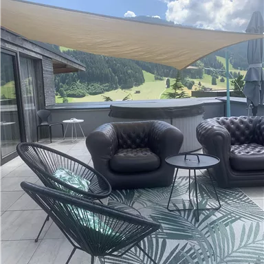 Eine elegante Terrasse mit modernen Möbeln und Blick auf eine grüne Landschaft. Die Atmosphäre ist einladend und entspannt, perfekt für sonnige Tage.
