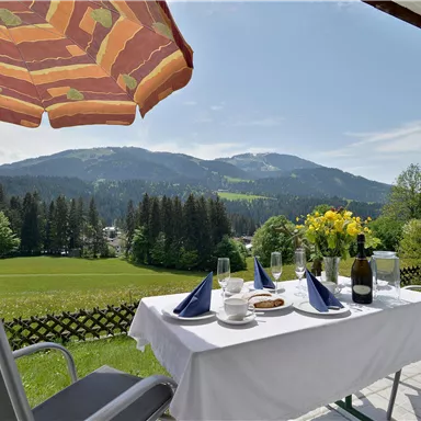 A beautiful outdoor table with a view of the mountains. On the table are flowers, wine, and a few snacks.