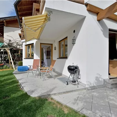 A cozy outdoor area with garden furniture. In the background, there is a swing and a grill visible.