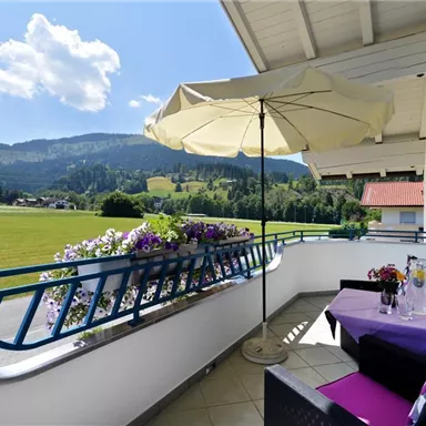 A beautiful balcony with a sunshade and blooming plants. In the background, there are hills and a blue sky.