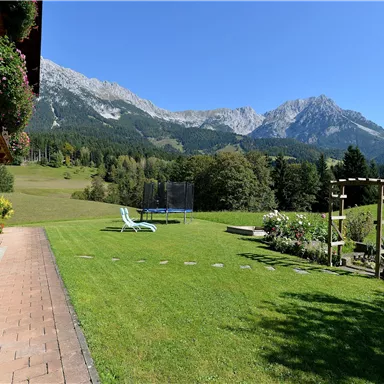 Eine Landschaft mit einem gepflegten Garten und Blick auf die Berge. Der Himmel ist klar und blau, ideal für einen entspannten Tag im Freien.