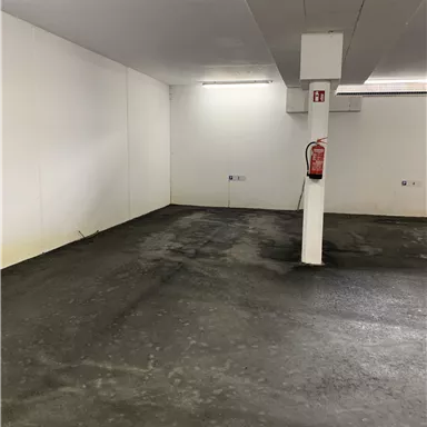 An empty room with a concrete floor and white walls. A fire extinguisher hangs on the wall.