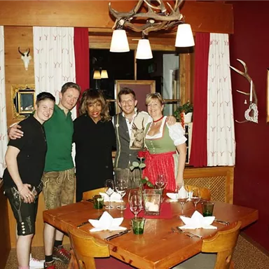 A group of five people is posing in a cozy restaurant. The table is lovingly set, and the walls are decorated with traditional pictures.