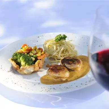 A delicious plate with chicken, vegetables, and spaghetti in a sauce. In the foreground, a glass of red wine.