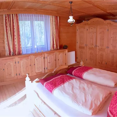 Ein gemütliches Schlafzimmer mit Holzvertäfelungen und roten Akzenten. Es gibt zwei Betten und einen geräumigen Kleiderschrank.
