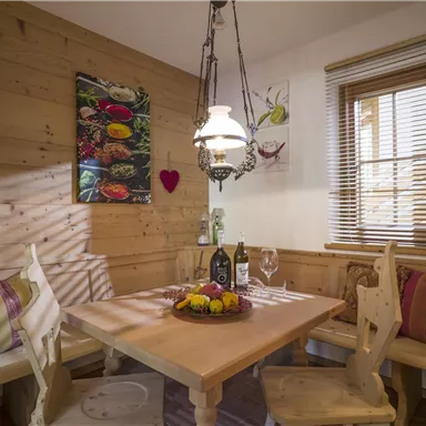 Ein gemütlicher Essbereich mit Holzmöbeln und warmem Licht. Auf dem Tisch stehen eine Flasche Wein und eine Obstschale.