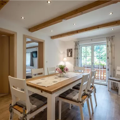A cozy dining area with a large table and bright chairs. The room has large windows and wooden ceilings that create an inviting atmosphere.