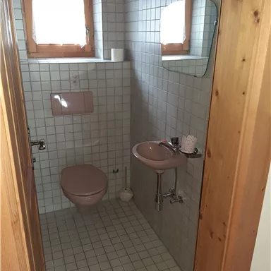 A small bathroom with light tiles and a shower. There is a sink and a toilet in soft colors.