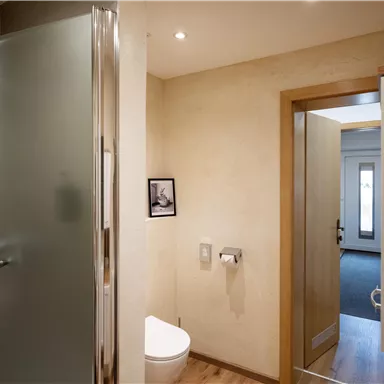 A modern bathroom with a shower and a toilet. The walls are in neutral colors, and the floor is made of wood.