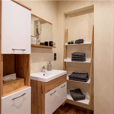 A modern bathroom with wooden shelves and a white sink.
Towels are neatly stacked and the walls have a neutral shade.