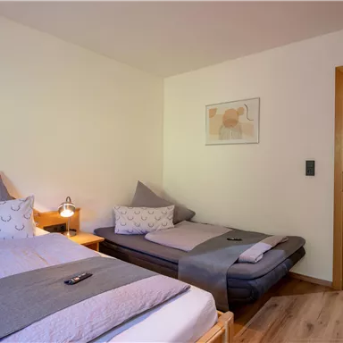 A cozy bedroom with two beds and bright walls. A window and a wooden frame create an inviting atmosphere.