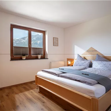 A cozy bedroom with a large bed and soft colors. Through the window, you can see a beautiful mountain landscape.