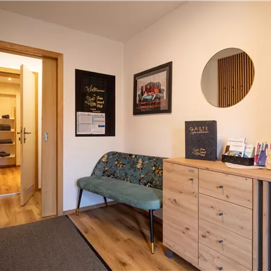 A modern hallway with wooden flooring and a green bench. Pictures and information are hanging on the wall, and a round mirror is also present.