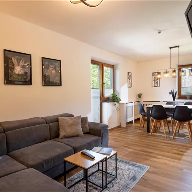 A modern living room with a comfortable couch and beautiful wooden floor. In the background, there is a dining area with a large table and chairs.
