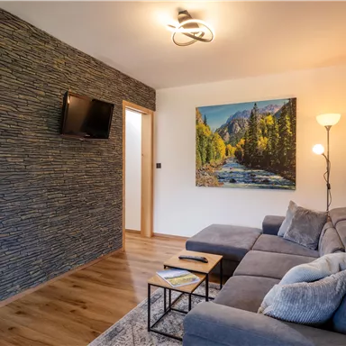 A stylish living room with a gray sofa and wooden floor. On the wall hangs a painting of a mountain landscape and there is a TV.