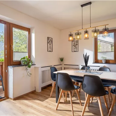 A bright dining room with a modern table and chairs. Large windows offer a view of the outside landscape.