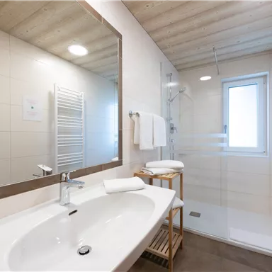 Ein modernes Badezimmer mit einem großen Waschbecken und einer Dusche. Helle Farben und Holzdetails schaffen eine einladende Atmosphäre.