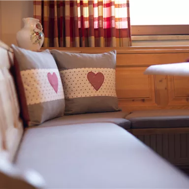 A cozy seating area with a gray sofa and cushions featuring red hearts. Striped curtains hang at the window, creating a warm atmosphere.