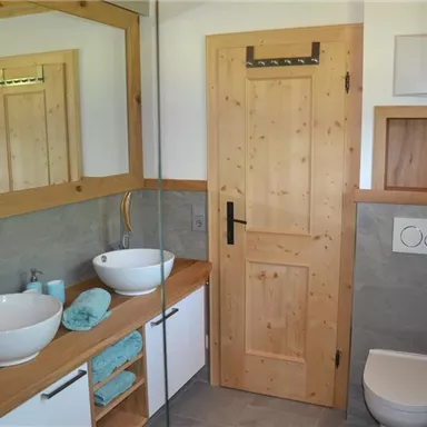 A modern bathroom with wood details and a large mirror. There are two sinks, plenty of storage space, and a bright, inviting atmosphere.