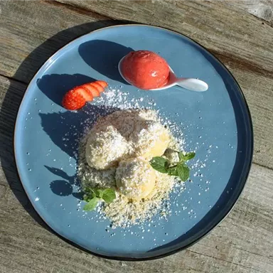 An elegant dessert presentation with two scoops of creamy ice cream, garnished with coconut flakes, fresh mint leaves, and a strawberry. Accompanied by a spoonful of fruity sorbet.