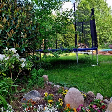 Ein schöner Garten mit bunten Blumen und einem Trampolin. Die Umgebung ist grün und einladend.