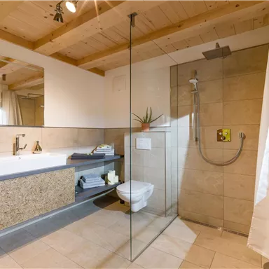 A modern bathroom with a large shower and a freestanding bathtub. The ceiling is made of wood and there are bright tiles on the floor.