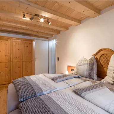 A cozy bedroom with two beds and a wooden ceiling. The room has a wardrobe and soft lighting.
