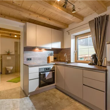A modern kitchen with wooden shelves and a bright countertop. The room is well-lit and designed entirely in neutral colors.