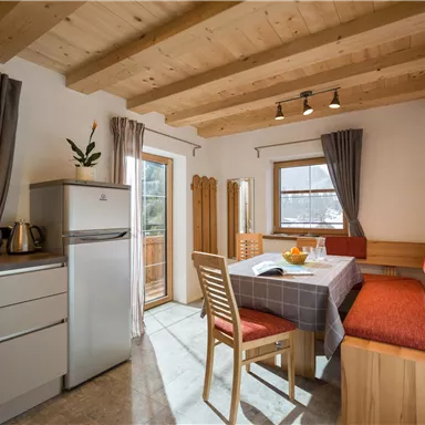 A bright and cozy kitchen with a dining table and wood design. There is a refrigerator and a pleasant seating area with windows that let in natural light.