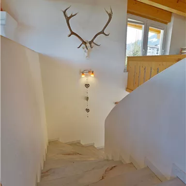 A bright staircase with a wooden railing and a deer antler on the wall. The room has large windows that let in natural light.