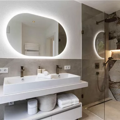 Ein modernes Badezimmer mit einem eleganten Waschbecken und einem großen Spiegel. Die Wände sind in sanften Erdtönen gehalten, und es gibt eine Dusche mit Glaswand.