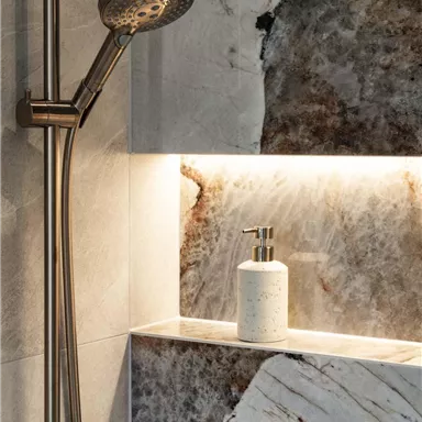 Eine elegante Dusche mit einem modernen Duschkopf und einer stilvollen Ablage. Die Wände sind aus schönem Marmor mit sanfter Beleuchtung.