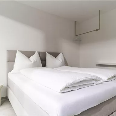 Ein modernes Schlafzimmer mit einem großen Bett und zwei Kopfkissen. Die Wände sind hell und der Raum wirkt hell und einladend.