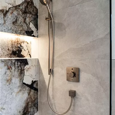 Eine moderne Dusche mit einer eleganten Handbrause. Die Wände sind mit grauem und marmoriertem Fliesen gestaltet.