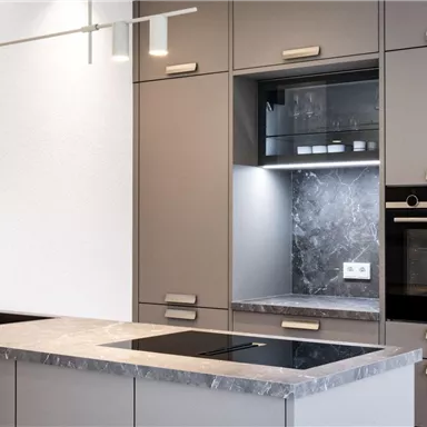 Eine moderne Küche mit grauen Schränken und einer eleganten Arbeitsplatte. Sie verfügt über einen eingebauten Ofen und Glasregale mit Beleuchtung.