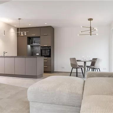 Eine moderne Küche mit einem Essbereich und einem bequemen Sofa. Der Raum hat helle Wände und viel natürliches Licht.
